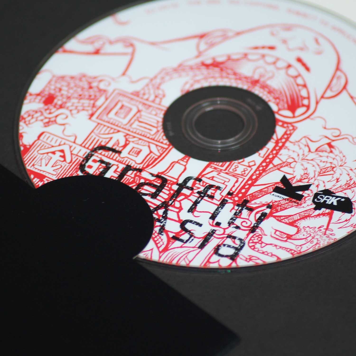 Close-up of a DVD from 'Graffiti Asia.' The DVD features intricate red and white artwork similar to the book's cover, with the title 'Graffiti Asia' and logos for SRK and Laurence King.