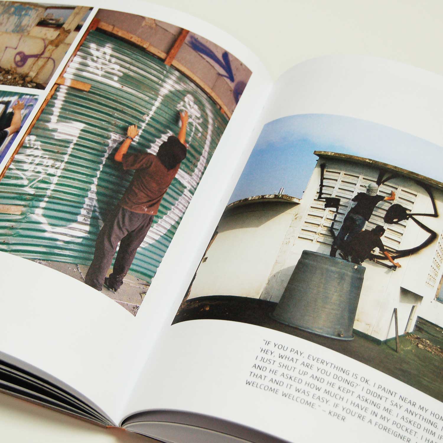 Open book from 'Graffiti Asia' showing two pages with photos of graffiti artists. The left page features an artist spray painting on a green shutter door. The right page shows another artist working on a wall, with a quote below about painting near home and interactions with police.